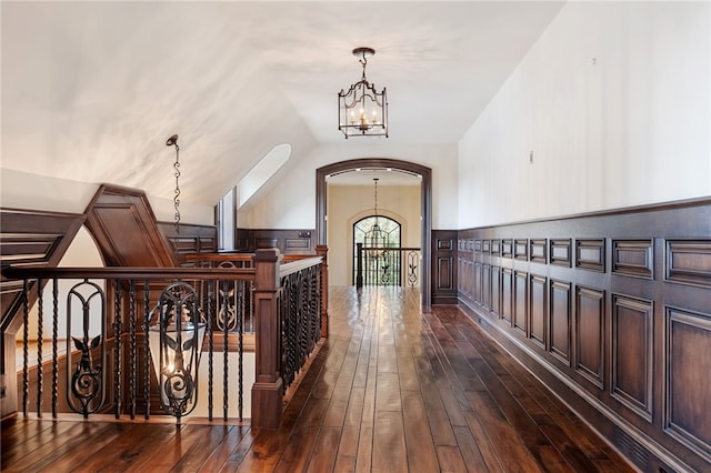 hallway featuring visible vents, dark wood-style flooring, a chandelier, vaulted ceiling, and an upstairs landing