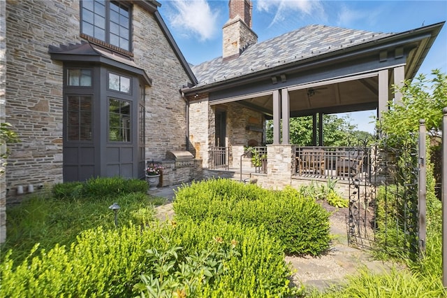 doorway to property with covered porch, stone siding, a high end roof, a chimney, and area for grilling