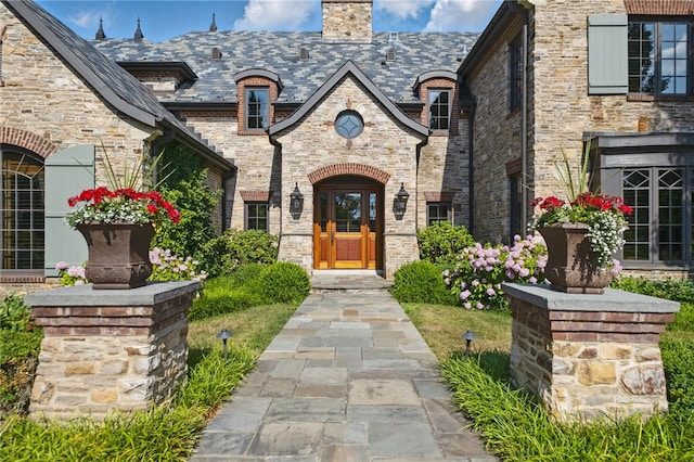 property entrance with brick siding, a high end roof, a chimney, and stone siding
