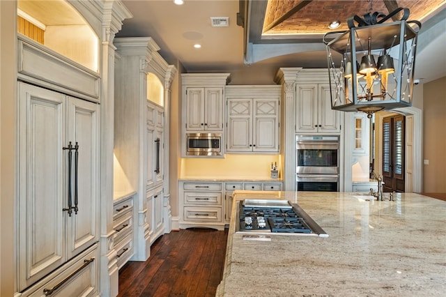 kitchen featuring light stone counters, built in appliances, a chandelier, dark wood-type flooring, and visible vents