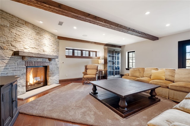 living area featuring baseboards, beamed ceiling, a stone fireplace, and wood finished floors