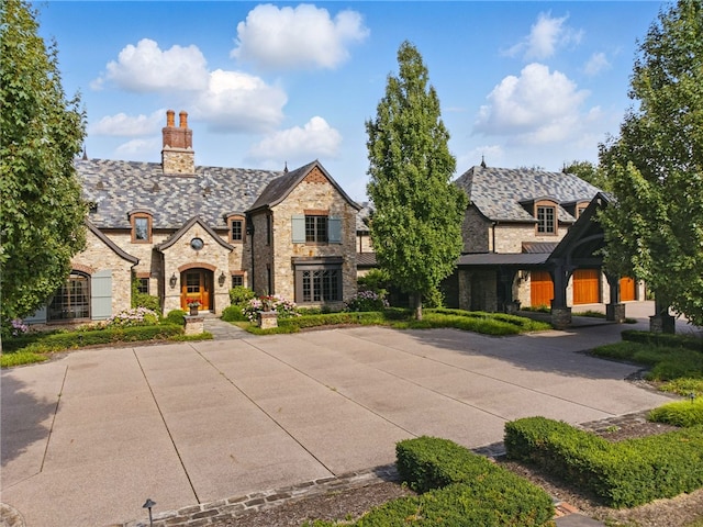 tudor house with a chimney, a high end roof, and stone siding