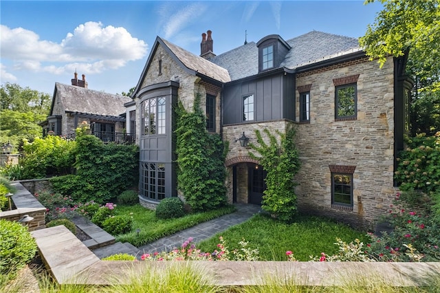 view of front of home with a high end roof, board and batten siding, a chimney, and stone siding
