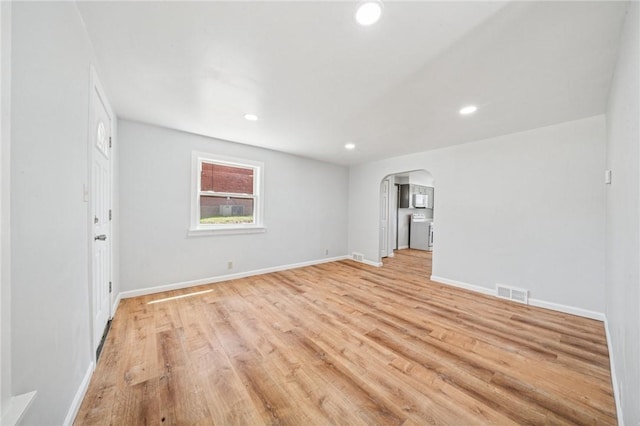 empty room with arched walkways, light wood-style flooring, recessed lighting, baseboards, and visible vents