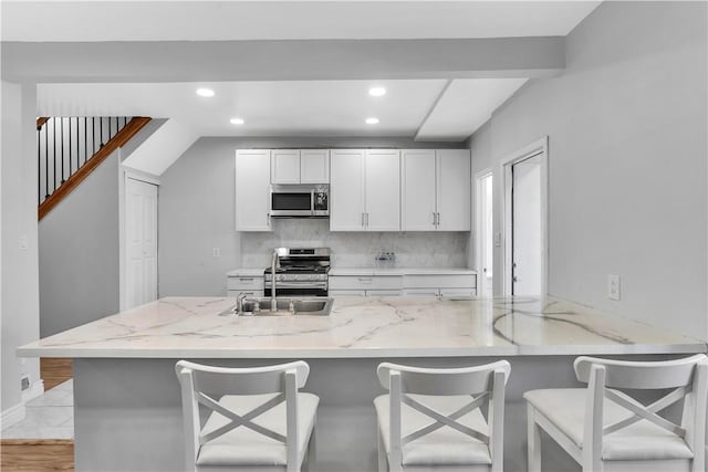 kitchen with backsplash, appliances with stainless steel finishes, light stone counters, recessed lighting, and white cabinetry