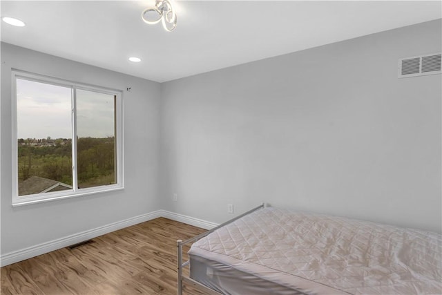 bedroom with baseboards, recessed lighting, wood finished floors, and visible vents