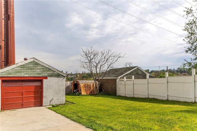 view of yard with concrete driveway, fence, an outbuilding, and a detached garage