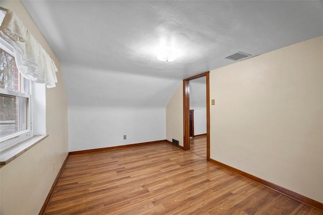 bonus room with baseboards, lofted ceiling, light wood-style flooring, and visible vents