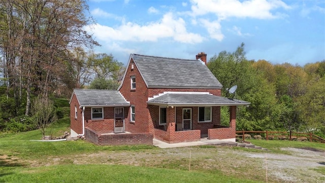 exterior space featuring a porch, a chimney, a lawn, brick siding, and fence