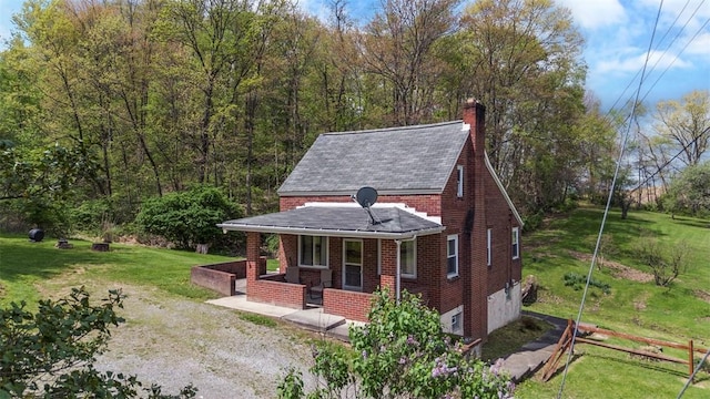 view of front of home featuring a porch, brick siding, a front lawn, and a chimney