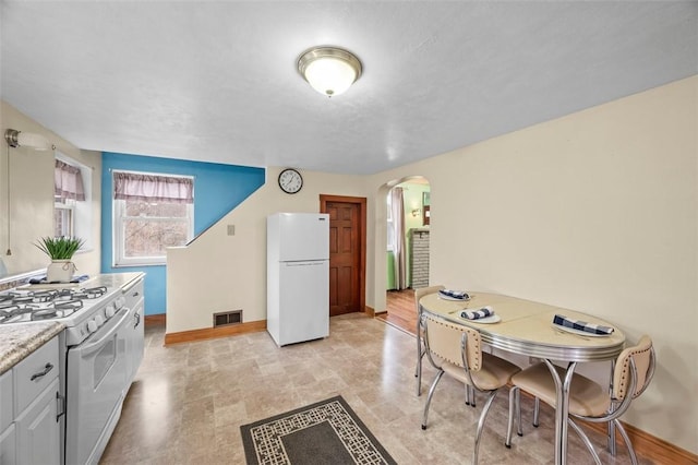 kitchen featuring white appliances, arched walkways, light countertops, baseboards, and visible vents