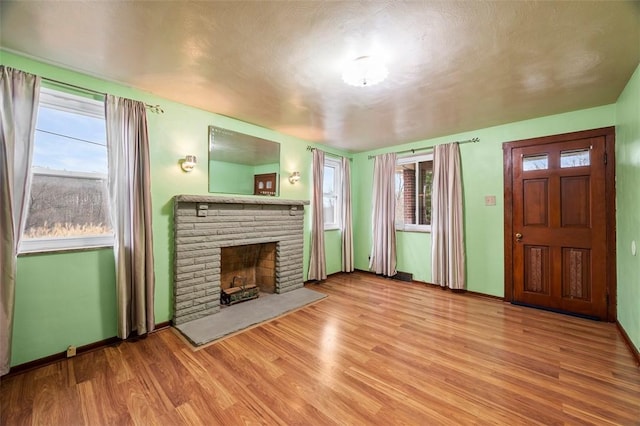 unfurnished living room featuring baseboards, a brick fireplace, and wood finished floors