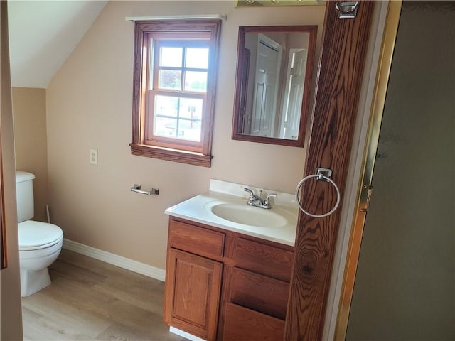 bathroom with vanity, toilet, baseboards, wood finished floors, and vaulted ceiling