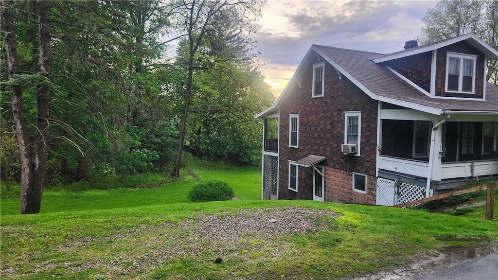property exterior at dusk featuring a chimney, a sunroom, cooling unit, a yard, and a shingled roof