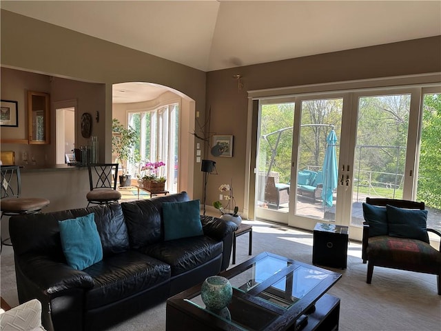 living area with carpet flooring, arched walkways, french doors, and lofted ceiling
