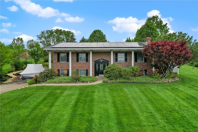 raised ranch with brick siding, solar panels, a chimney, and a front lawn