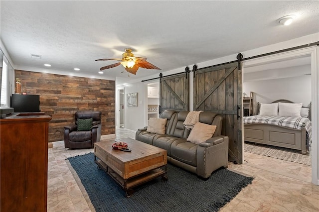 living room featuring ceiling fan, visible vents, wood walls, a barn door, and recessed lighting