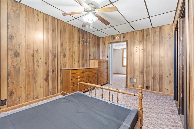 carpeted bedroom with wooden walls, ceiling fan, and visible vents