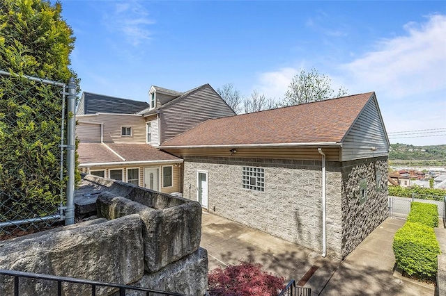 rear view of house featuring stone siding, fence, a shingled roof, and a patio area