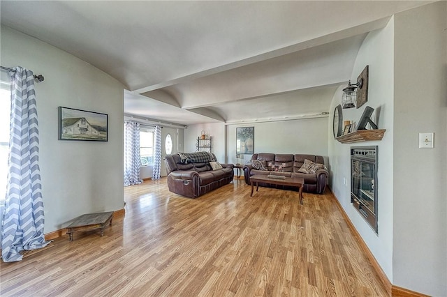 living room with baseboards, a glass covered fireplace, and light wood-style floors