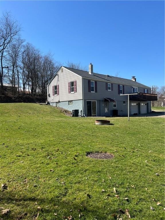 back of house with cooling unit, a yard, a chimney, an attached garage, and driveway