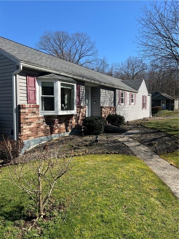 view of front of house featuring brick siding, roof with shingles, and a front yard