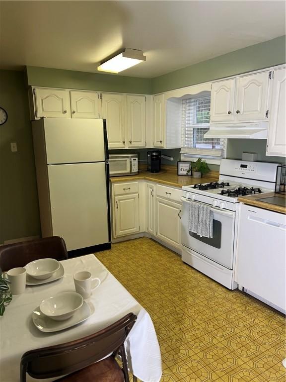 kitchen with white appliances, white cabinets, under cabinet range hood, and light floors