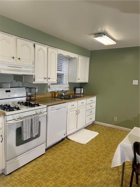 kitchen with white appliances, light floors, under cabinet range hood, white cabinets, and a sink