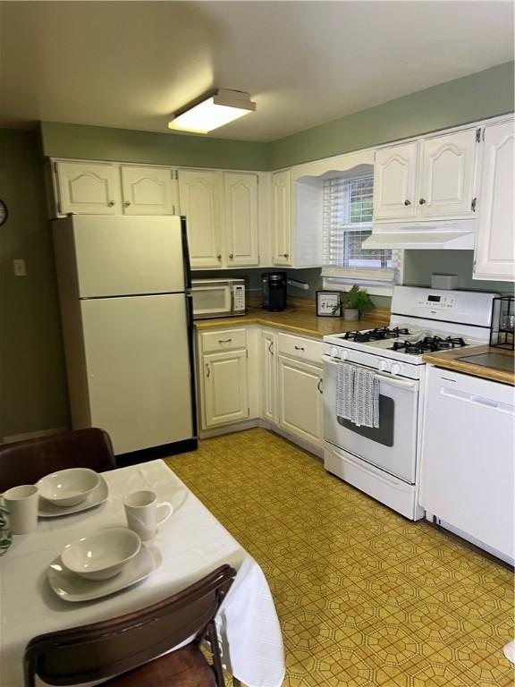 kitchen with light floors, white cabinets, under cabinet range hood, and white appliances