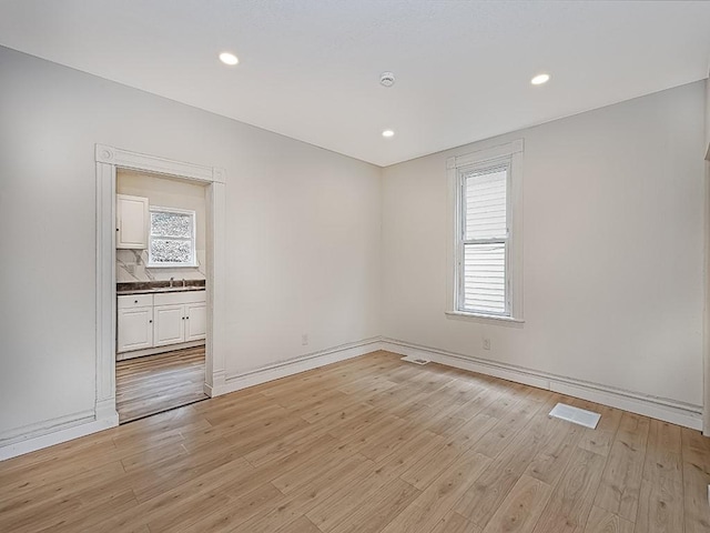 unfurnished room with visible vents, baseboards, recessed lighting, light wood-type flooring, and a sink