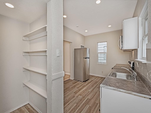 kitchen with appliances with stainless steel finishes, open shelves, light wood-type flooring, a sink, and baseboards