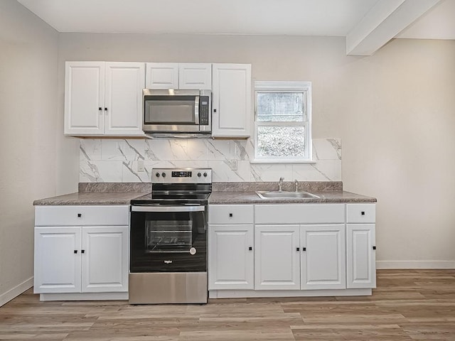 kitchen featuring white cabinets, stainless steel appliances, baseboards, and a sink