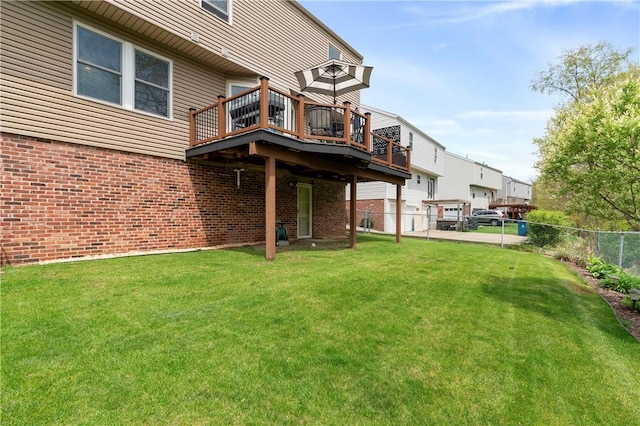 rear view of house with fence, a yard, a deck, and brick siding