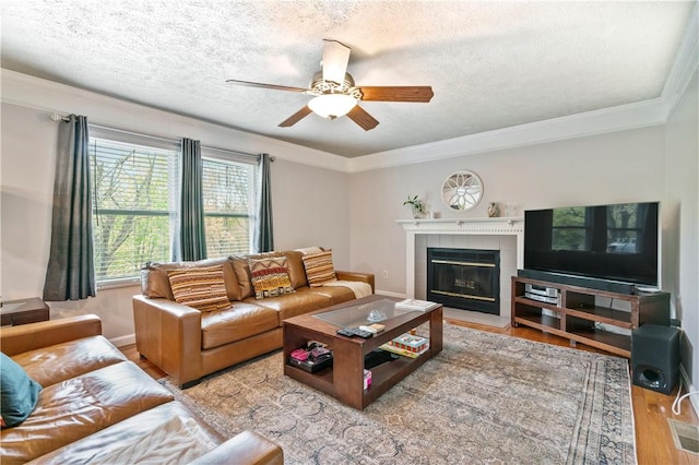 living area with crown molding, wood finished floors, a textured ceiling, a tile fireplace, and a ceiling fan