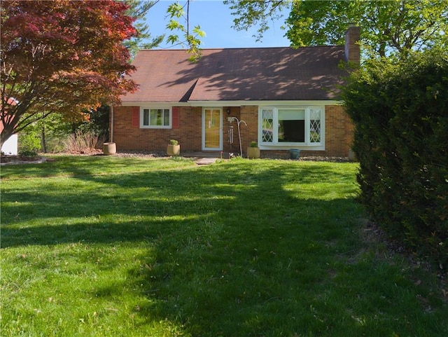 view of front of property featuring brick siding, a front yard, and a chimney