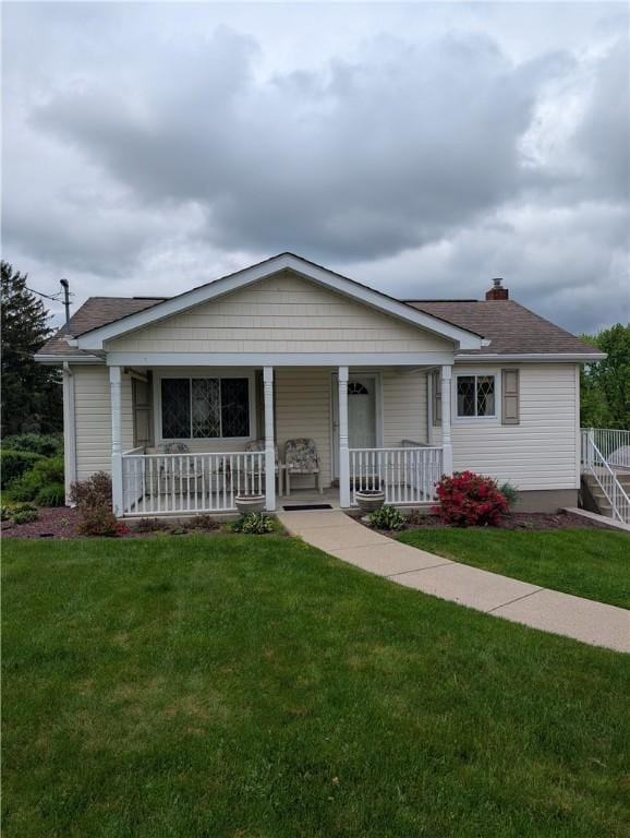view of front of house with roof with shingles, covered porch, and a front lawn