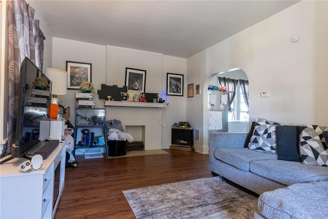 living room with a fireplace with flush hearth, arched walkways, and wood finished floors