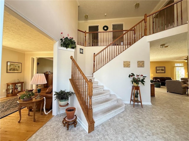 stairway featuring a textured ceiling, ornamental molding, and a high ceiling
