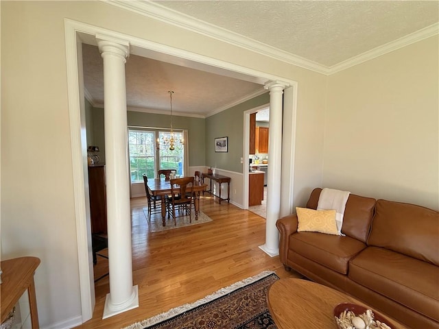 living room featuring an inviting chandelier, ornamental molding, decorative columns, a textured ceiling, and light wood-style flooring