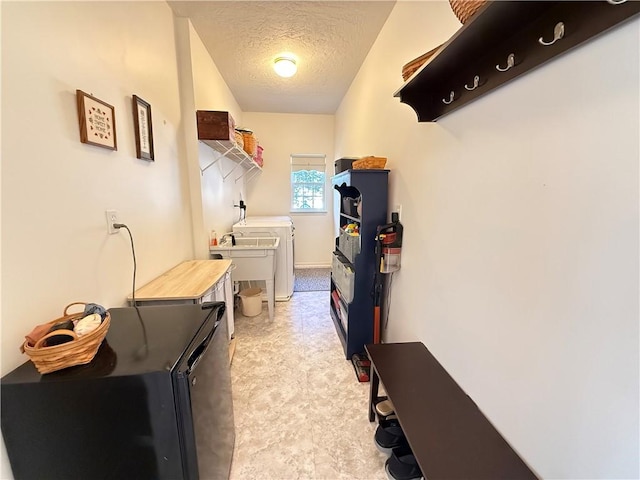 laundry area with laundry area, light floors, a textured ceiling, washing machine and clothes dryer, and a sink