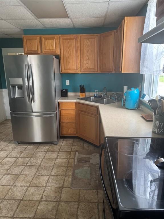 kitchen with brown cabinetry, range, light countertops, a sink, and stainless steel fridge