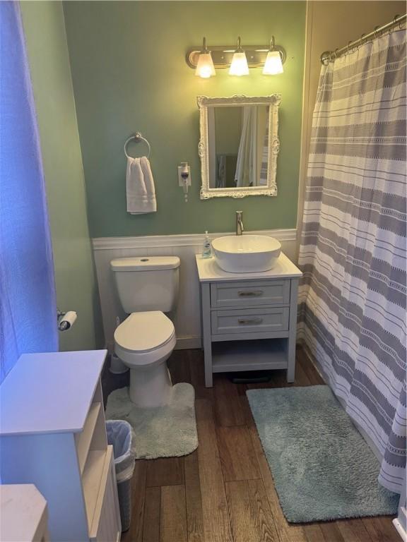 full bath featuring vanity, wood finished floors, toilet, and a wainscoted wall