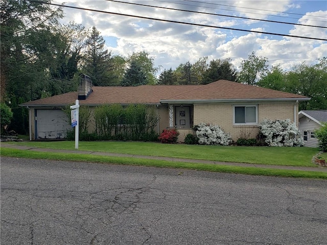 ranch-style home featuring a shingled roof, a front lawn, brick siding, a garage, and a chimney