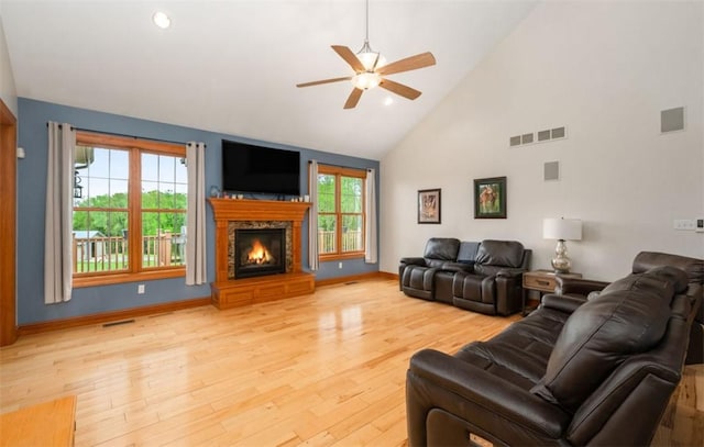 living room featuring a ceiling fan, a stone fireplace, visible vents, high vaulted ceiling, and light wood finished floors
