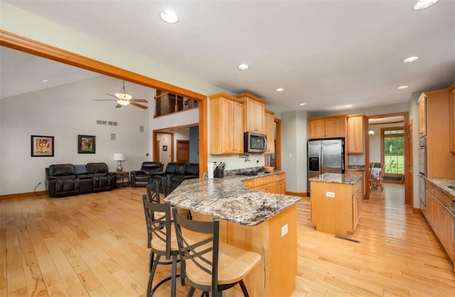 kitchen featuring light wood-style floors, a peninsula, appliances with stainless steel finishes, and light stone countertops
