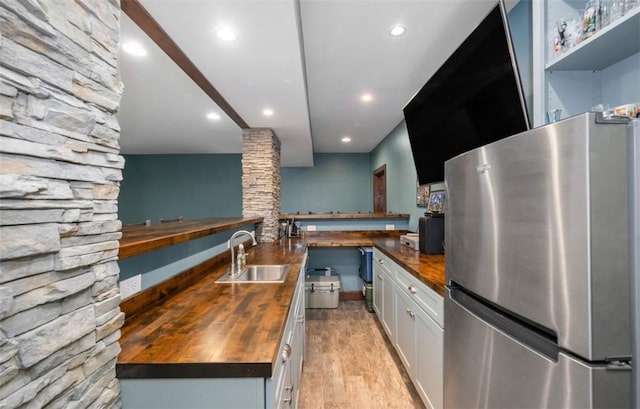 kitchen featuring a sink, wooden counters, freestanding refrigerator, recessed lighting, and white cabinetry