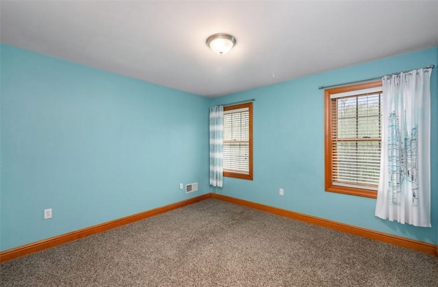 carpeted spare room featuring visible vents, baseboards, and a healthy amount of sunlight