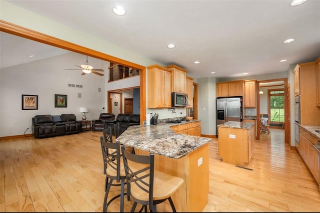 kitchen with appliances with stainless steel finishes, a center island, light wood-type flooring, and light stone counters