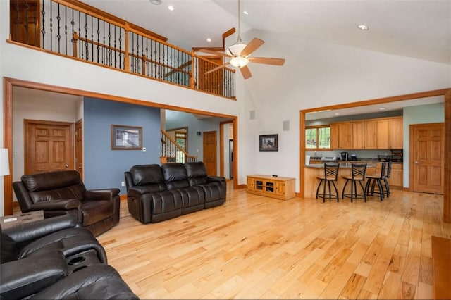 living room featuring ceiling fan, stairs, high vaulted ceiling, light wood-style floors, and recessed lighting