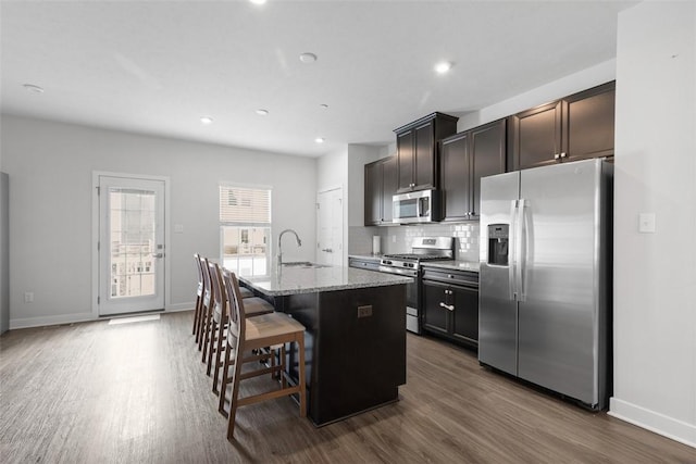 kitchen featuring a sink, stainless steel appliances, light stone counters, a kitchen island with sink, and dark wood finished floors